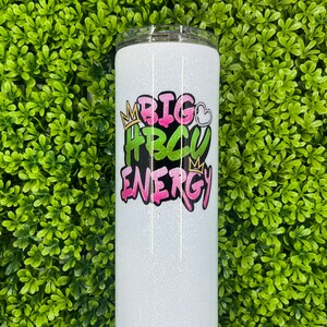 May include: White glitter tumbler with a pink, green, and black graphic that says "BIG HBCU ENERGY" with crowns on either side.