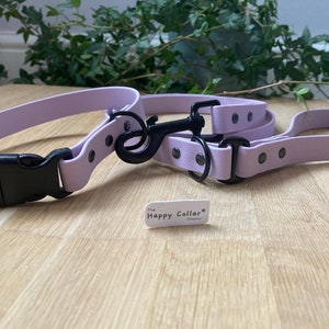 Op de afbeelding: Een lavendelkleurige hondenhalsband en riemset met zwarte hardware en een klein label met de tekst "The Happy Collar Company".