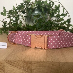 May include: A pink and white polka dot dog collar with a rose gold buckle. The collar is made of fabric and has a metal D-ring. The collar is labeled "The Happy Collar Company".
