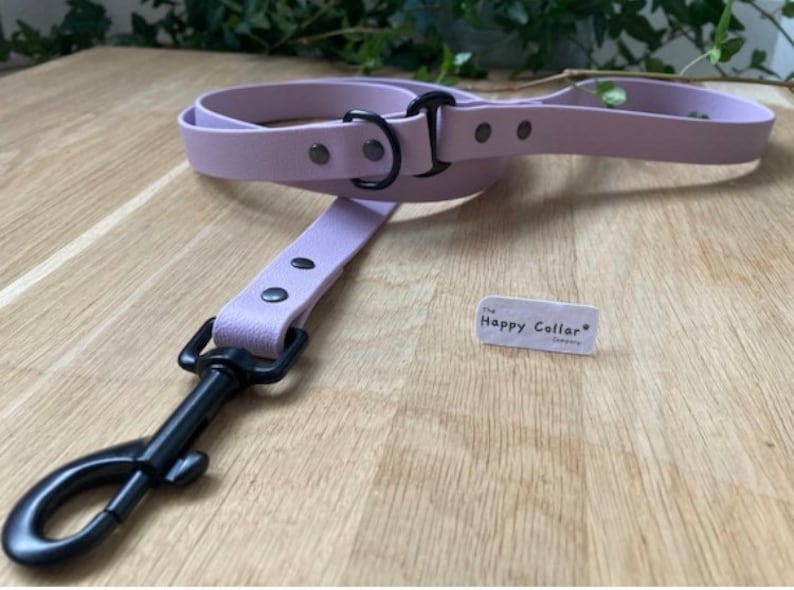 May include: A lavender leather dog leash with black hardware and a black metal clip. The leash has a tag that says "The Happy Collar Company".