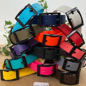 May include: A stack of colorful rubber dog collars with black buckles. The collars are in various colors, including blue, green, orange, red, purple, pink, yellow, and gray. The collars are arranged in a pile, with the buckles facing up. The text "The Happy Collar Company" is visible at the bottom of the image.