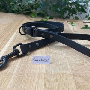May include: Black leather dog leash with a metal clasp and silver accents. The leash is on a wooden surface with a small white tag that says "The Happy Collar Company".