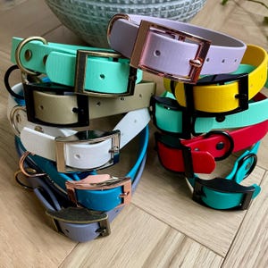 May include: A stack of colorful dog collars with different buckle styles. The collars are made of a rubber-like material and come in a variety of colors, including teal, white, yellow, red, and lavender.