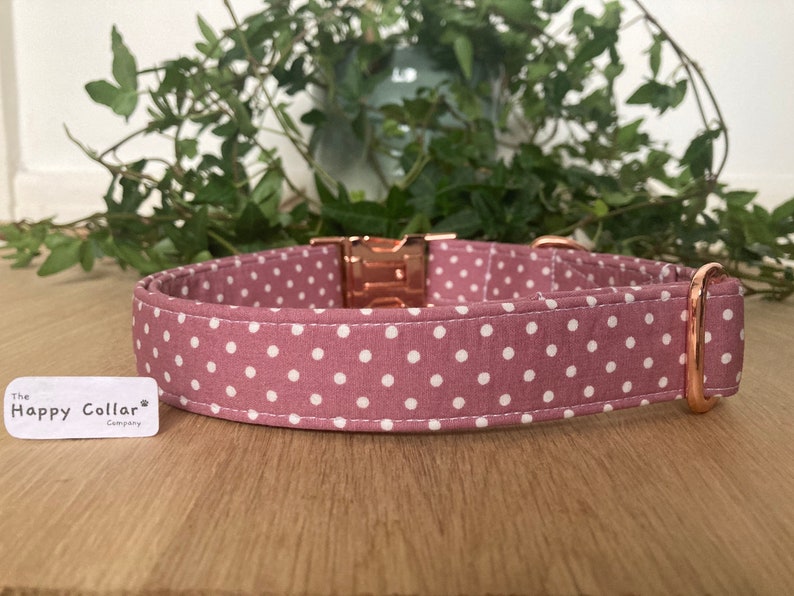 May include: A pink dog collar with white polka dots and rose gold hardware. The collar is made of fabric and has a buckle closure. The collar is labeled "The Happy Collar Company."