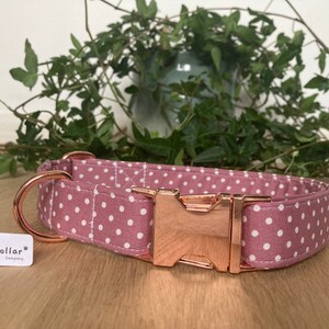 May include: A pink and white polka dot dog collar with a rose gold buckle and D-ring. The collar is made by The Happy Collar Company.