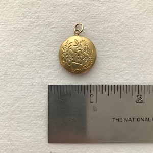 May include: A gold locket with a floral design. The locket is about 1 inch in diameter and has a loop for a chain.
