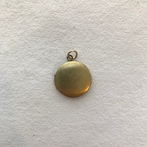 May include: A gold-toned locket pendant with a circular shape and a hinged opening. The locket has a smooth, polished surface.