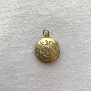 May include: A gold locket pendant with an engraved floral design. The locket is round and has a small loop at the top for attaching a chain.