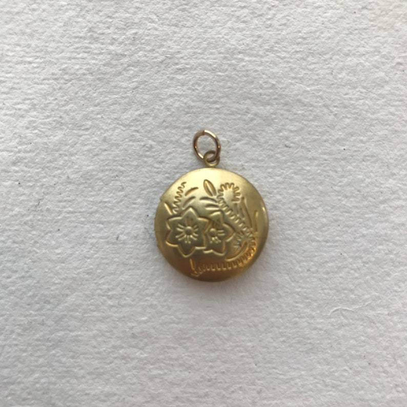 May include: A gold locket pendant with an engraved floral design. The locket is round and has a small loop at the top for attaching a chain.