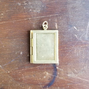 May include: A gold-toned locket with a hinged opening. The locket is rectangular and has a smooth surface.