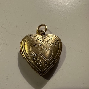 May include: A gold heart-shaped locket with an intricate design of two hearts and floral accents.