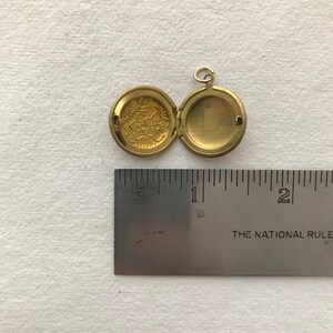 May include: A gold-toned locket with a floral design on the front and a blank interior. The locket is open and measures approximately 1 inch in diameter.