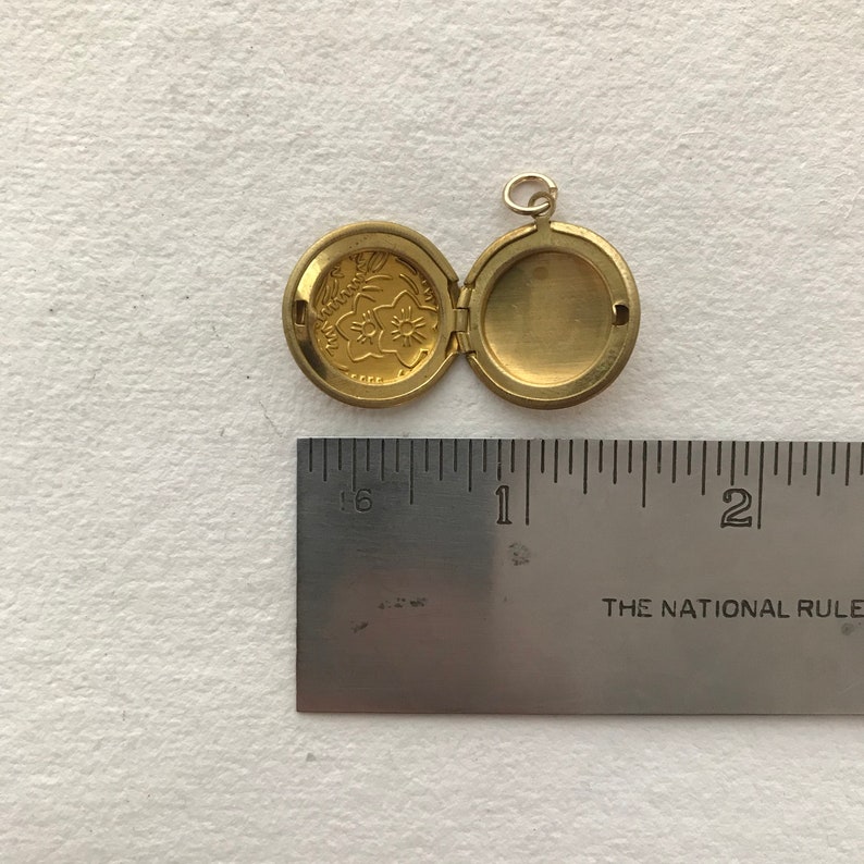 May include: A gold-toned locket with a floral design on the front and a blank interior. The locket is open and measures approximately 1 inch in diameter.