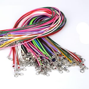 Pode incluir: Uma coleção de cordões encerados coloridos com fechos de lagosta prateados. Os cordões estão dispostos em uma pilha, com os fechos na parte inferior. Os cordões são de várias cores, incluindo vermelho, rosa, verde, azul e branco.