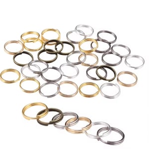 May include: A collection of split key rings in various metallic finishes, including gold, silver, and bronze. The key rings are arranged on a white surface, showcasing their circular shape and split design for easy attachment.