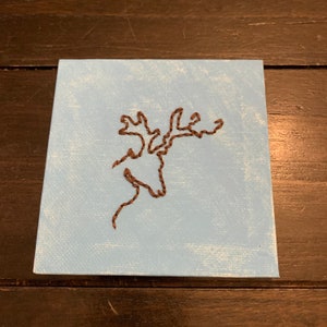 May include: Square canvas art with a brown embroidered moose head outline on a light blue background. The artwork is mounted on a square canvas, suitable for wall decor.