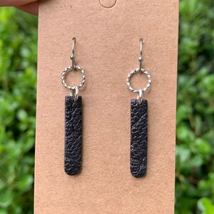 May include: A pair of black dangle earrings with a textured finish. The earrings have a silver hoop at the top and a silver hook.