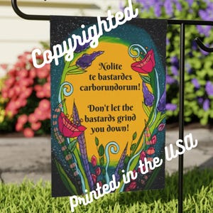 Puede incluir: Una bandera de jardín con fondo negro y diseño floral colorido. La bandera presenta el texto "Nolite te bastardes carborundorum! Don't let the bastards grind you down!" y "Printed in the USA."