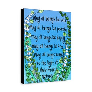 May include: A canvas art print with a blue background and black text that reads "May all beings be safe, peaceful, happy, free, awaken to the light of their true nature." Green and white vines frame the text.