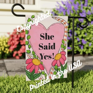 May include: A pink heart with the text "She Said Yes!" surrounded by flowers and a striped pattern. The text "Printed in the USA" is at the bottom of the image.