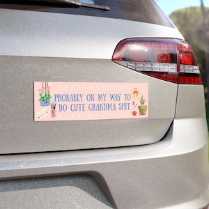 Può includere: Un magnete rettangolare rosa per auto con il testo blu "PROBABLY ON MY WAY TO DO CUTE GRANDMA SHIT". Il magnete presenta illustrazioni di una pianta sospesa, forniture per cucito e una pianta in vaso.