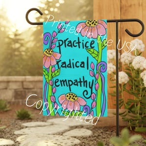 May include: A turquoise blue garden flag with pink flowers and green leaves. The text on the flag reads "Practice Radical Empathy".