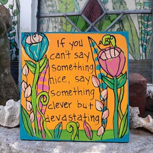 May include: Square wooden sign with an orange background and teal border. The sign features a hand-painted design of flowers and leaves, with the text "If you can't say something nice, say something clever but devastating."