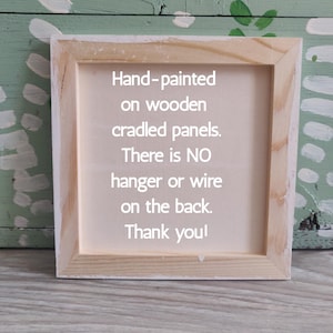May include: A square, wooden-framed canvas with the text "Hand-painted on wooden cradled panels. There is NO hanger or wire on the back. Thank you!" The frame is made of light-colored wood.