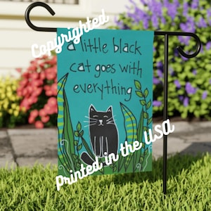 May include: A teal garden flag with the text "a little black cat goes with everything" and a black cat illustration. The flag is printed in the USA and features a black metal stand.