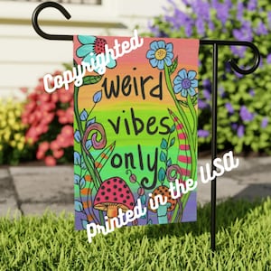 Puede incluir: Una colorida bandera de jardín con el texto "weird vibes only" en una fuente caprichosa. La bandera presenta un fondo degradado de arcoíris, flores, setas y el texto "Printed in the USA".