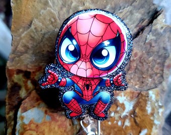 May include: A red and blue cartoon Spider-Man character with a black glitter background on a retractable badge holder.