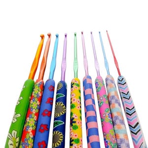 May include: A set of nine crochet hooks with colorful patterned handles. Each hook features a unique design, including floral, sunflower, checkered, and chevron prints in various colors like green, orange, blue, yellow, pink, and red.