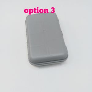 May include: A rectangular, light gray plastic storage case with rounded corners and a smooth, solid surface. The text "option 3" is printed in bold, bright pink letters above the case. The container features a simple, functional design.
