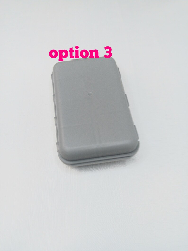 May include: A rectangular, light gray plastic storage case with rounded corners and a smooth, solid surface. The text "option 3" is printed in bold, bright pink letters above the case. The container features a simple, functional design.