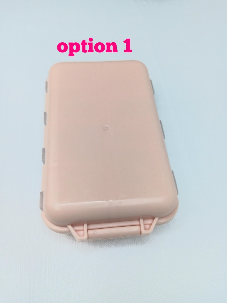 May include: A rectangular, light pink plastic storage case with rounded corners and a hinged lid. The text "option 1" is printed in pink above the case. The container features a secure latch mechanism on the front edge and visible side hinges.