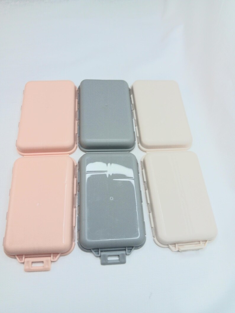 May include: Six rectangular plastic storage cases arranged in two rows of three. The top row features one light pink, one gray, and one beige case. The bottom row contains one light pink, one gray, and one beige case, each with a small latch.