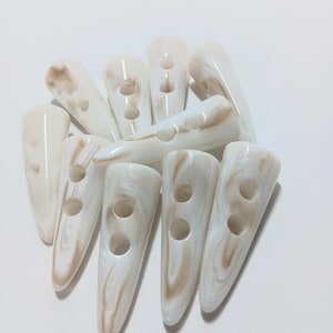 May include: A group of ten white and brown plastic buttons with two holes each. The buttons are shaped like a pointed cone.