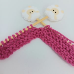 May include: Two wooden knitting needles with pink yarn and white sheep-shaped stitch markers.