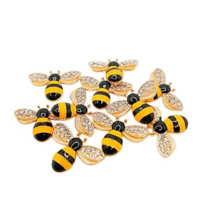 May include: A collection of bee-shaped charms featuring black and yellow enamel stripes on the bodies and clear rhinestones embedded in the wings. Each charm has a gold-toned metal outline, creating a uniform appearance across the group.