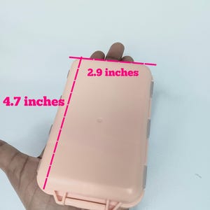 May include: A rectangular, light peach-colored plastic storage case with a hinged lid and secure latch. The case features pink measurement lines and text indicating dimensions of 2.9 inches in width and 4.7 inches in length on the exterior.