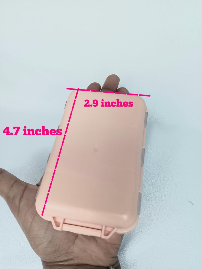 May include: A rectangular, light peach-colored plastic storage case with a hinged lid and secure latch. The case features pink measurement lines and text indicating dimensions of 2.9 inches in width and 4.7 inches in length on the exterior.