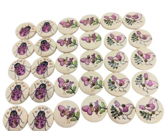 May include: A collection of round, light-colored wooden buttons featuring printed illustrations. The designs include purple ladybugs with small hearts and pink birds perched on green leafy branches. Each button has two holes for sewing.