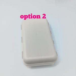 May include: A rectangular, light gray plastic storage case with rounded corners and a smooth surface. The text "option 2" is printed in pink above the case. The container features a hinged design with visible side latches for secure closure.