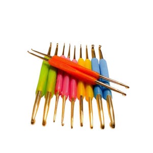 May include: A collection of double-ended crochet hooks featuring gold-toned metal tips and textured plastic handles in vibrant colors including lime green, bright pink, yellow, orange, and light blue, arranged in a fan-like cluster.
