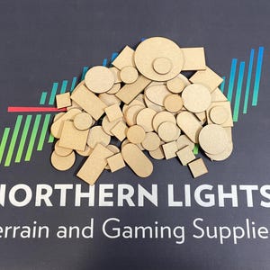 May include: A large assortment of wooden circles and squares in various sizes. The pieces are all a light brown colour and are arranged in a pile. The text "NORTHERN LIGHTS Terrain and Gaming Supplies" is visible at the bottom of the image.