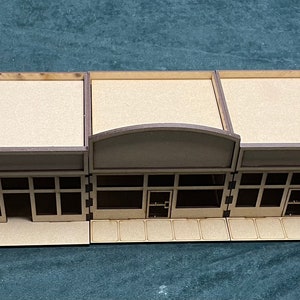 May include: A set of five brown wooden storefront facades with arched windows and doors. The facades are designed for use in miniature model building or tabletop gaming.