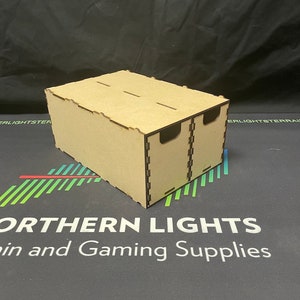 May include: A wooden box with two compartments, each with a separate opening. The box is made of light brown wood and has a smooth finish. The box is sitting on a black surface with a green and red striped pattern.