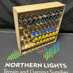 May include: A wooden paint bottle storage rack with 72 slots. The rack is filled with rows of small paint bottles with various coloured lids. The rack is made of light brown wood and has a natural finish.
