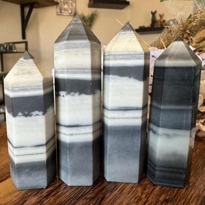 Könnte beinhalten: Vier kristalltürme mit grau-weißen Streifen werden auf einer Holzoberfläche präsentiert. Die Kristalle haben eine sechseckige Form und sind in einer Reihe angeordnet. Die Kristalle sind etwa 10 bis 18 cm hoch.