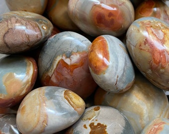 May include: A pile of polished stones in shades of brown, orange, grey, and cream. The stones are smooth, rounded, and glossy, with distinctive patterns and veining. Each stone has a unique appearance.